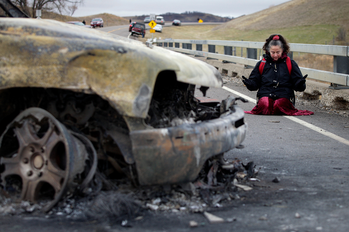 Sandra O'Connor of Bainbirdge Island, Wash. prays next to a charred vehicle located in front of a law enforcement barricade on N.D. Highway 1806 near the Dakota Access Pipeline construction site north of Cannon Ball, North Dakota on October 29, 2016. 