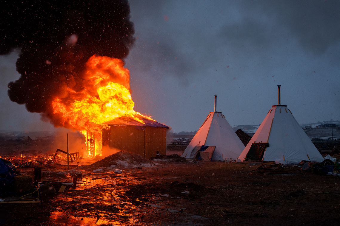 A Navajo hogan burns next to a row of tarpees early Wednesday morning at the Oceti Sakowin campground. 