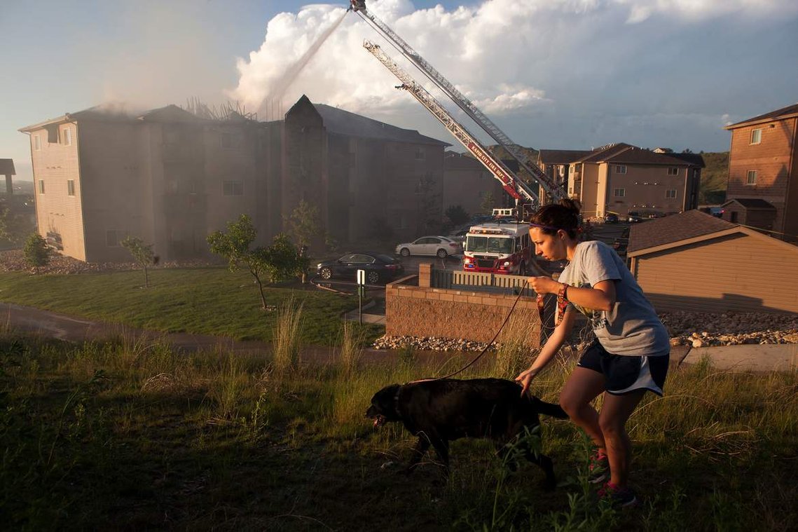 Paula Martin walks her dog across a hill overlooking an apartment fire on Saturday, June 21 at the Stoney Creek Highlands Apartment Homes in Rapid City. Lightning is believed to have caused the fire, which left nearly 30 residents without a home.