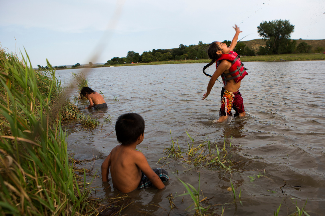 Peta One Feather, 8, right, jumps out of the Cannonball River as he plays with his cousins Easton Condon, 4, and Achilles Condon, 3, Thursday, Sept. 1 at the Oceti Sakowin campsite.