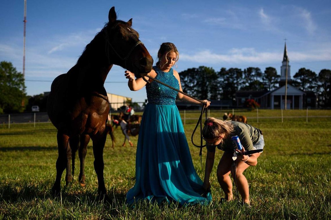 Sally Poteat holds her horse Newt still as Sydney Garrison adjusts her dress to take prom photos in the practice field after competing in a rodeo at the Crescent High School FFA Arena Saturday, May 1, 2021.