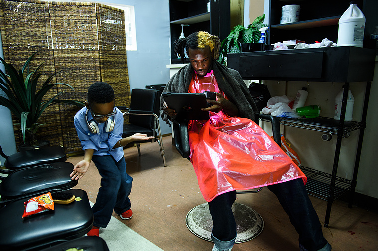 Robbie Johnson, 7, dances next to his father Isaih Kinloch as he waits for him to set a game up on his iPad at a salon in Summerville on Thursday, July 26, 2018.