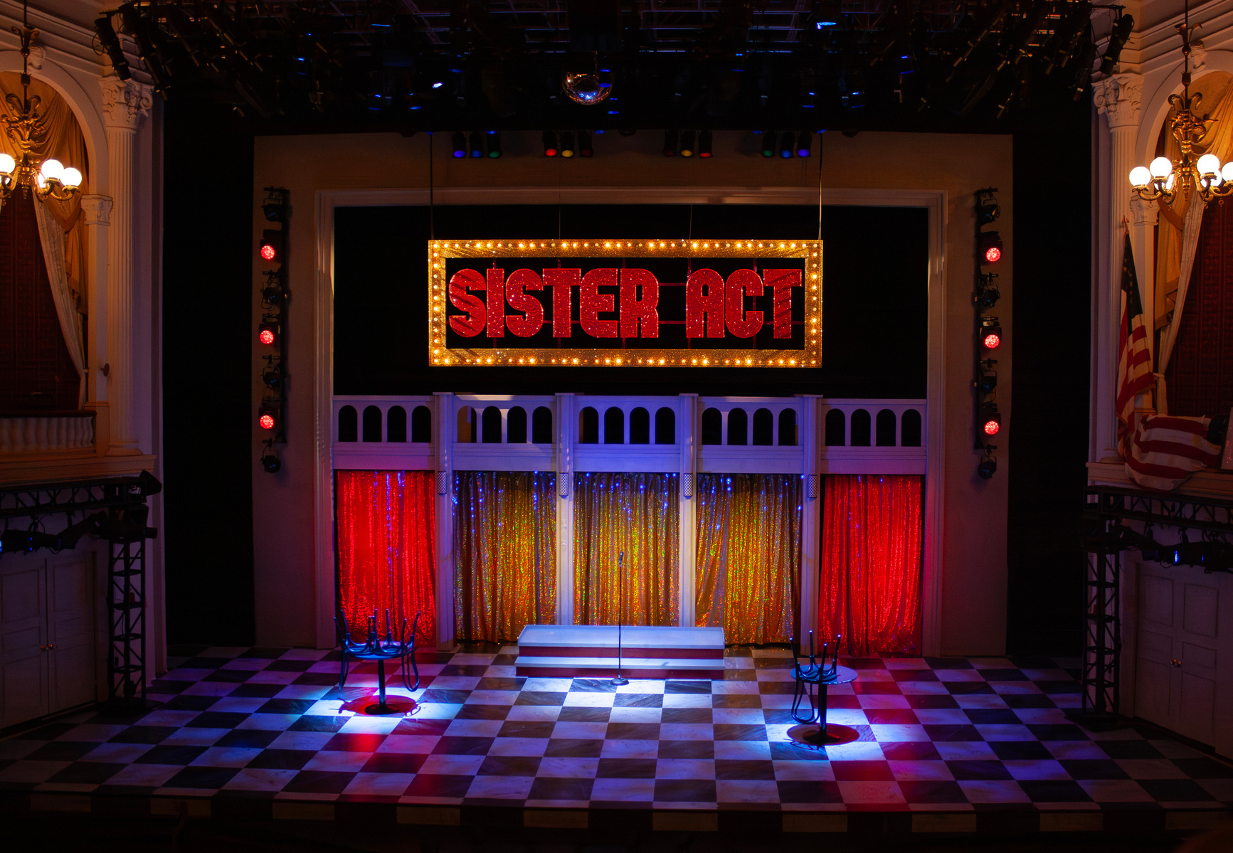 Paige Hathaway's scenic design for "Sister Act", directed by Jeff Calhoun at Ford's Theatre in 2025. The design consists of spinning panels, a large portal with theatrical lights, a checkerboard marble floor, and a backlit stained glass backdrop.
