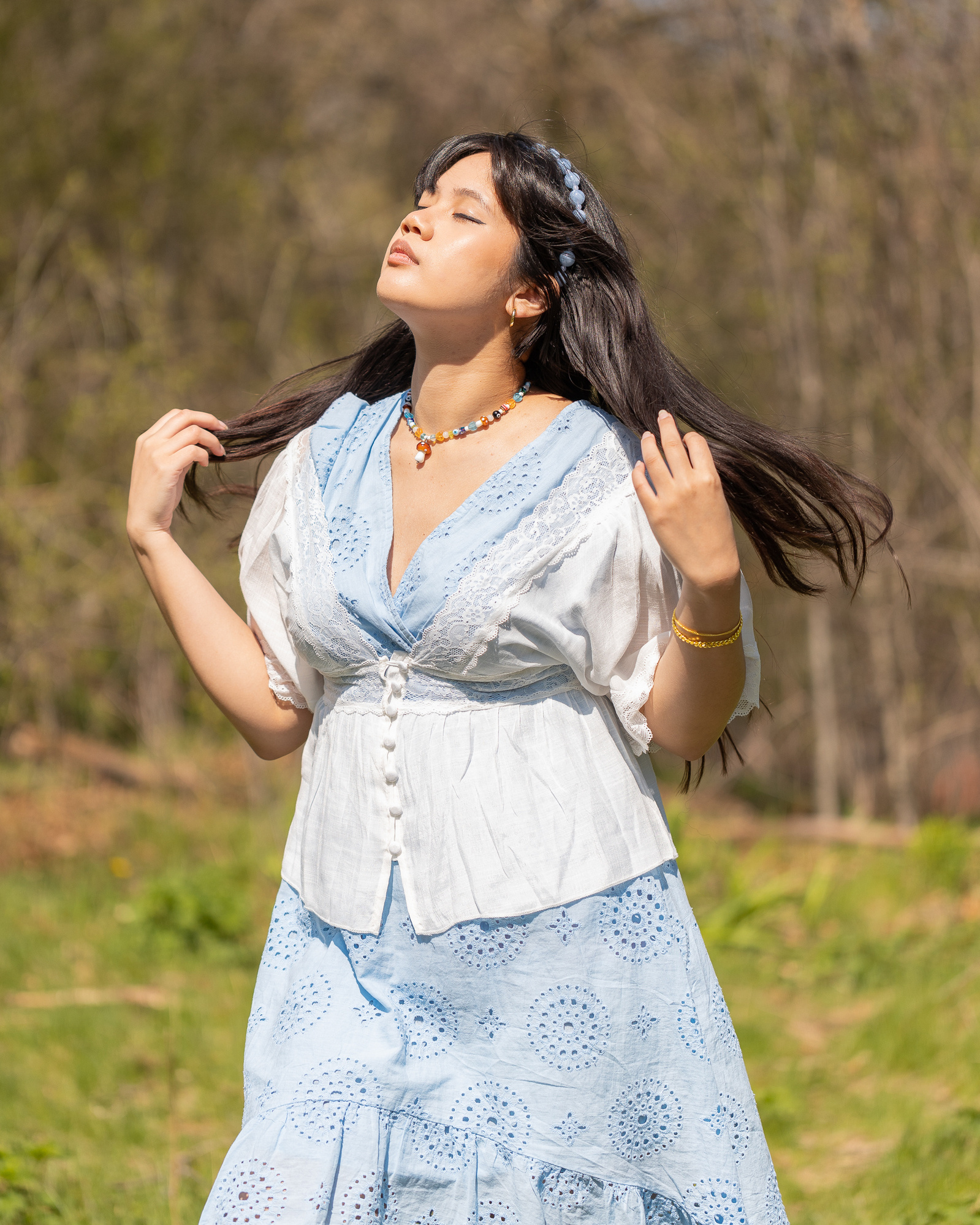Portrait of Asian woman looking towards sun with hair blowing in wind, wearing blue lacey dress.