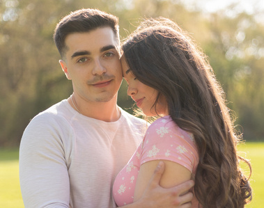 Close-up of couple standing in field. Woman resting her forehead on man's cheek while he looks towards camera.