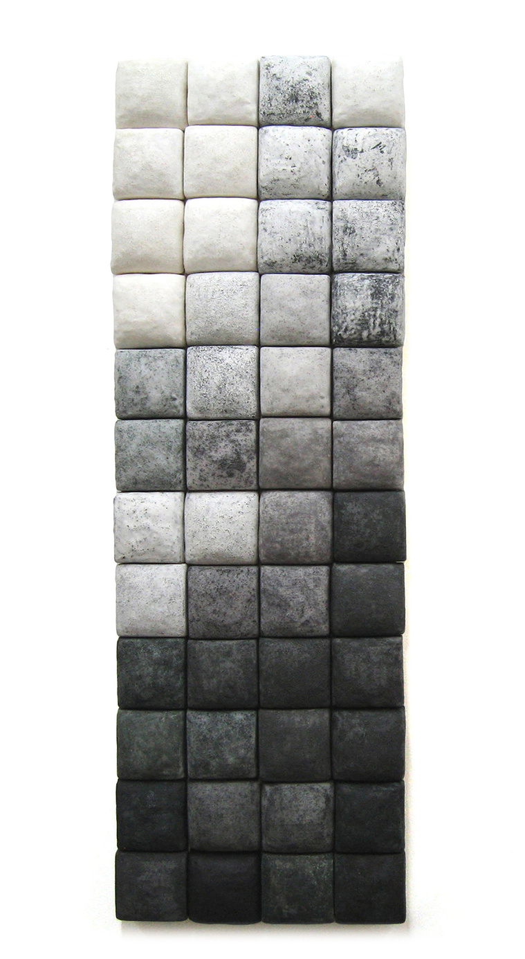 Ceramic squares mounted on a panel create the architectural installation titled Grey Scale. The two-inch squares graduate from whites through grays to blacks. The constructed piece of ceramic wall art was created by artist Kathy Erteman.