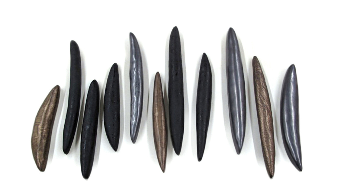 A balanced arrangement of sculpted stoneware pod forms create the Metallic Catalpa Pods ceramic wall sculpture by Kathy Erteman. The abstract shapes are glazed in metallic pewter, gold, and black to make this commissioned custom design luminous