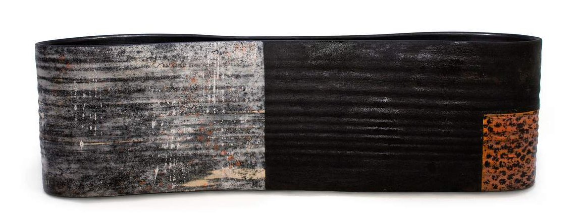 Squeeze Long Vessel is a minimal, modernist stoneware art piece by Kathy Erteman with a long, narrow, curved profile. The wheel-thrown and altered vessel is orange, white and black