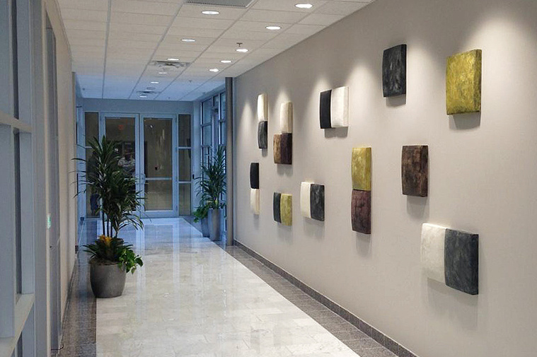 This image shows a ceramic wall installation titled In Balance, which Kathy Erteman created for the Tam Corporation in Texas. The 15-inch hand-built stoneware wall squares in black, white, ochre, brown, and grey textured glazes is a minimal design