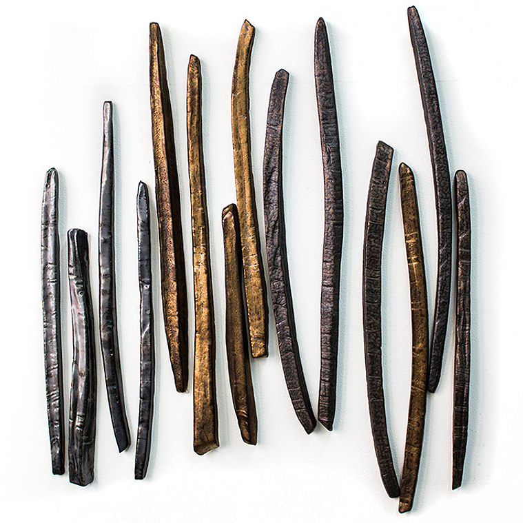 An artful arrangement of sculpted catalpa stick-pods in a vertical row make up the Catalpa Stix ceramic wall sculpture by Kathy Erteman. Made of stoneware, the wall-mounted installation has pewter and gold glazes inspired by nature