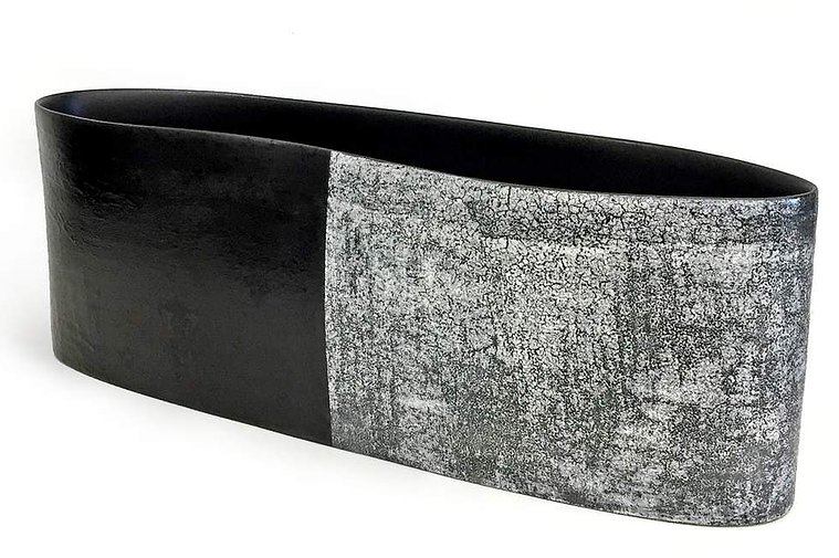 Wheel thrown and altered, Asphalt and Snow 3 by Kathy Erteman is a curved long vessel made of porcelain with a black texture slip and texture white glaze visually dividing the piece of art in half 