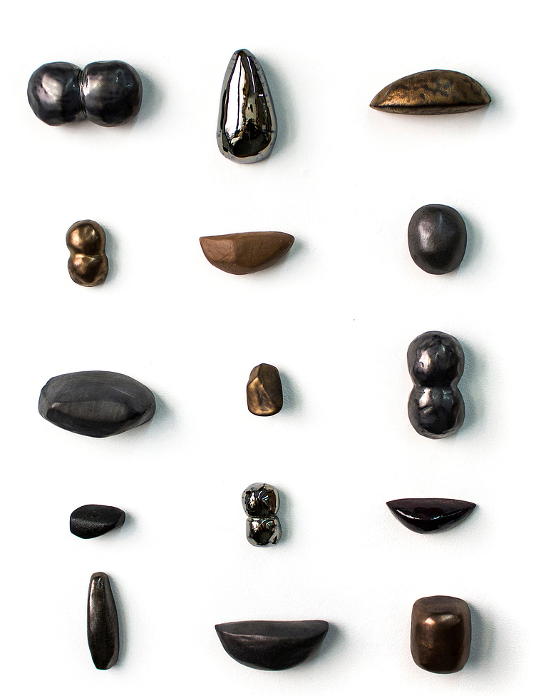 By artist Kathy Erteman, Curio Cabinet is a ceramic wall sculpture with porcelain sculpted forms based on nature in varying organic shapes. These pods have been glazed in gold, silver, and pewter to unify the elements in the ceramic wall piece