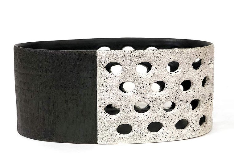 The Agra Long Vessel is a work of art by Kathy Erteman that has been wheel thrown and altered, then pierced and covered in a white texture glaze. The other section of the minimal ceramic form is contrasting in a textured black slip