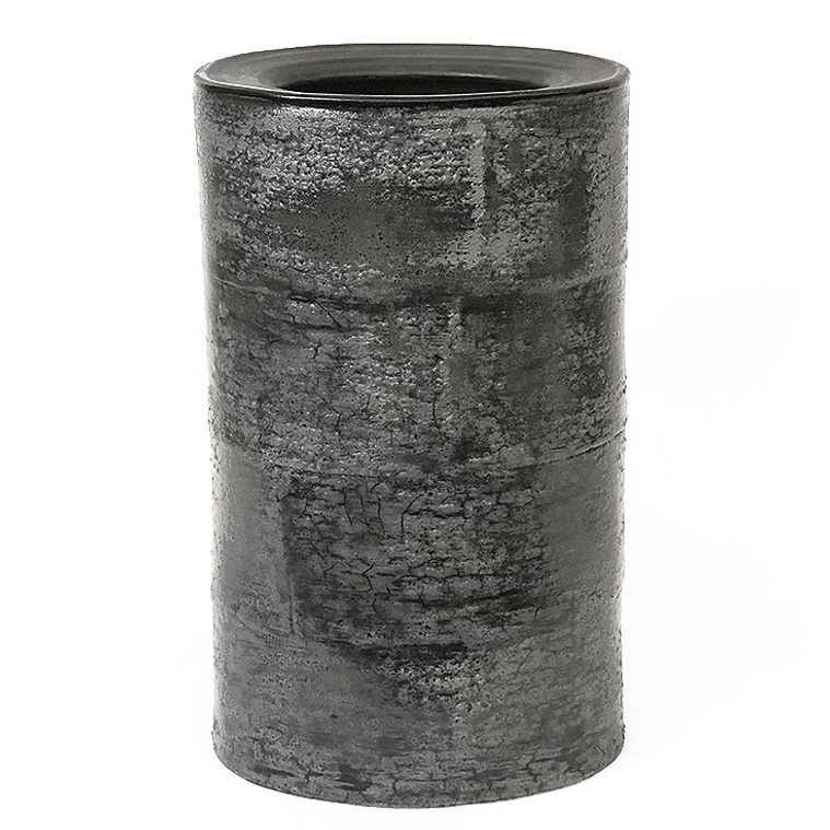 Kathy Erteman created the Grey Bark Drum Vessel. The hand-built stoneware sculpture has grey and black glazes, a tree bark texture, and covered top with a hole. This is an example of Erteman’s sculptural ceramics