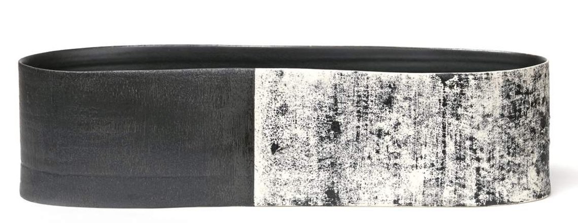 Artist Kathy Erteman created the Snow and Tar Long Vessel, a minimal, modern ceramic vessel that was wheel thrown and stretched. The black and white art piece has a texture glaze with an abstract monoprint detail