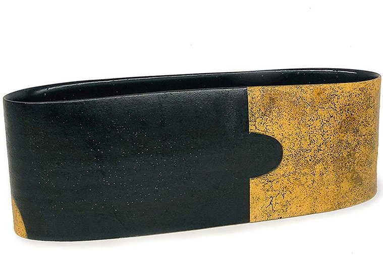 Kathy Erteman’s Tab Long Vessel is a work of art that has been thrown and altered, one portion covered in an ochre texture glaze and the other section of the long and narrow minimal form in black