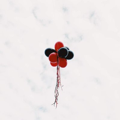 Floating in the sky on a cloudy day is a helium balloon topiary of red and black balloons