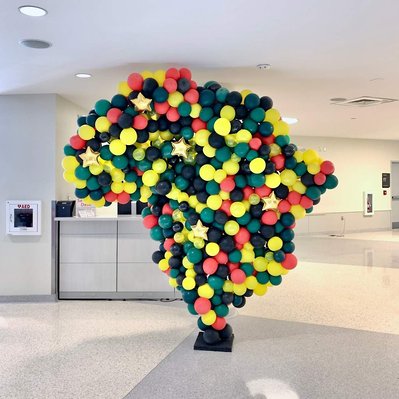 in a large white room is a large balloon sculpture in the shape of Africa in yellow black green and red balloons