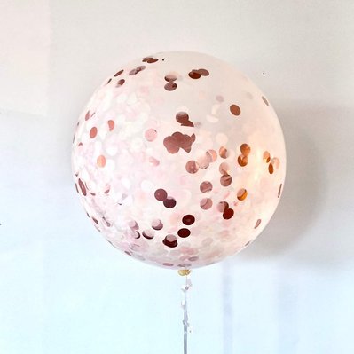In front of a white wall is a clear white balloon with rose gold confetti