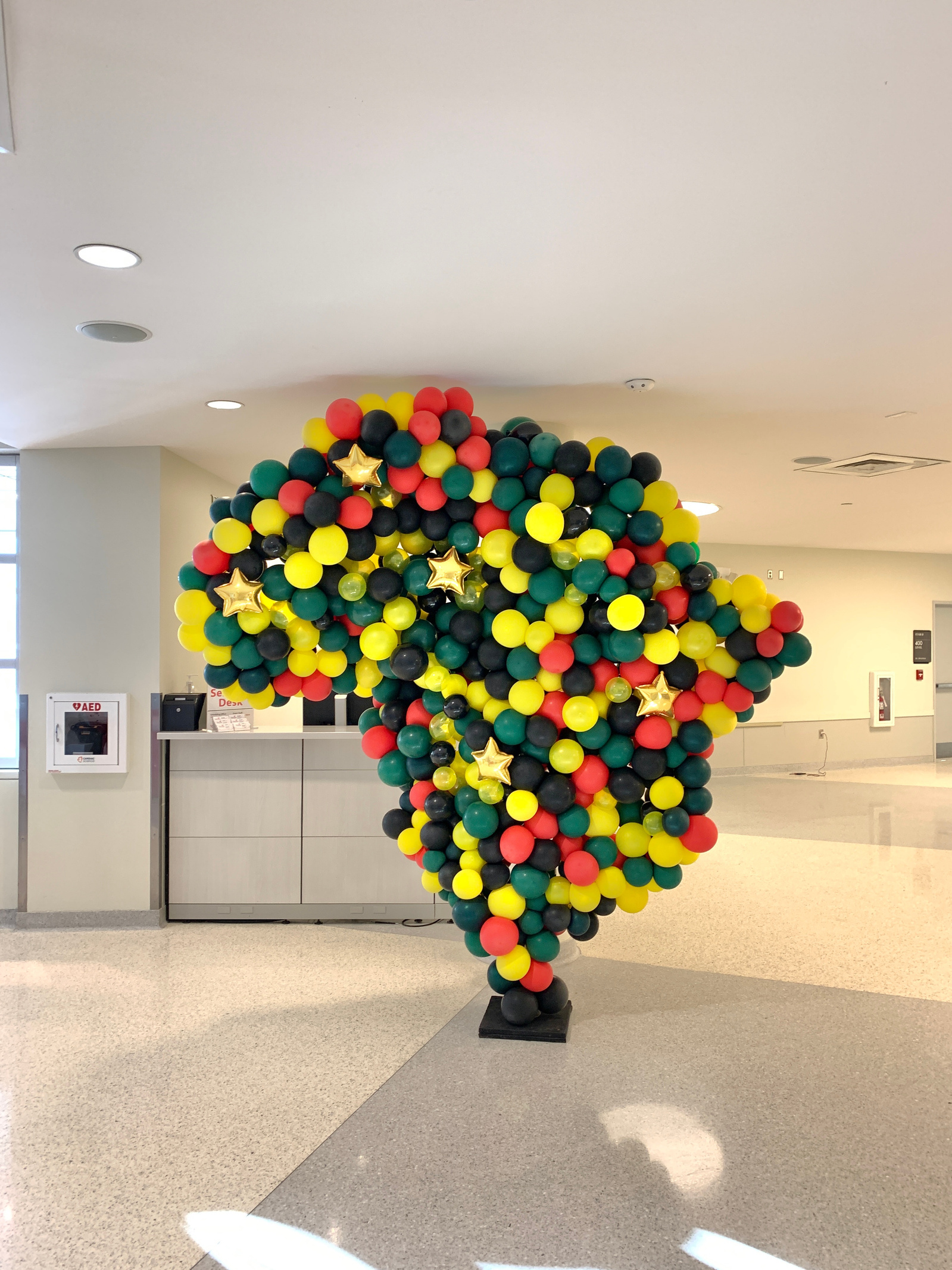 in a large white room is a large balloon sculpture in the shape of Africa in yellow black green and red balloons
