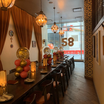 A long brown table is decorated with balloon centerpieces of gold pink and confetti balloons