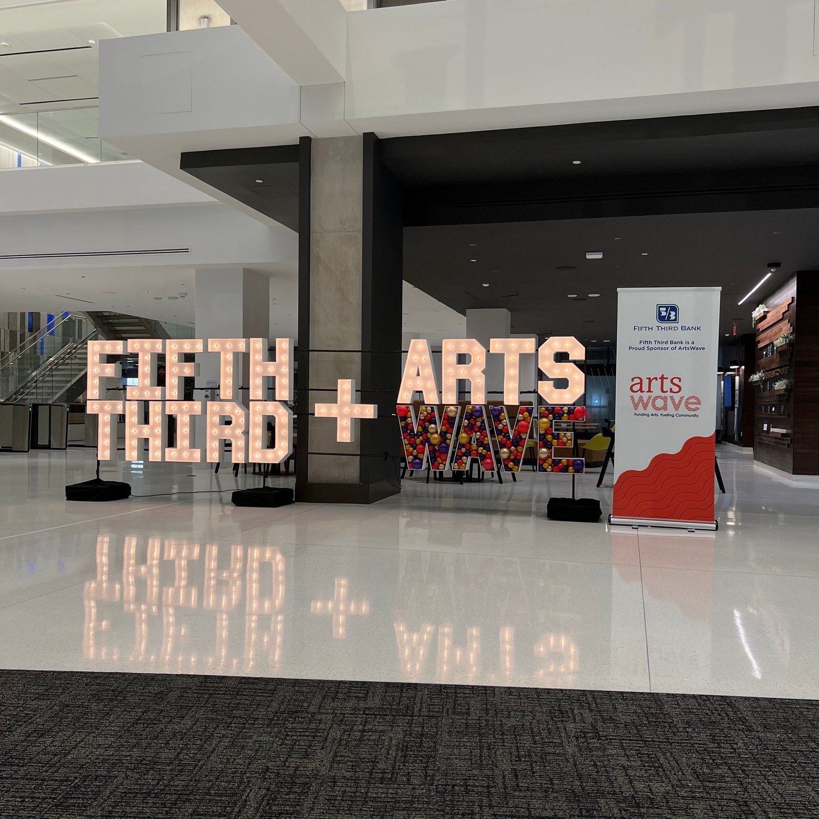 In a large open white room are light up marquee letters with balloon mosaic letters next to an event sign
