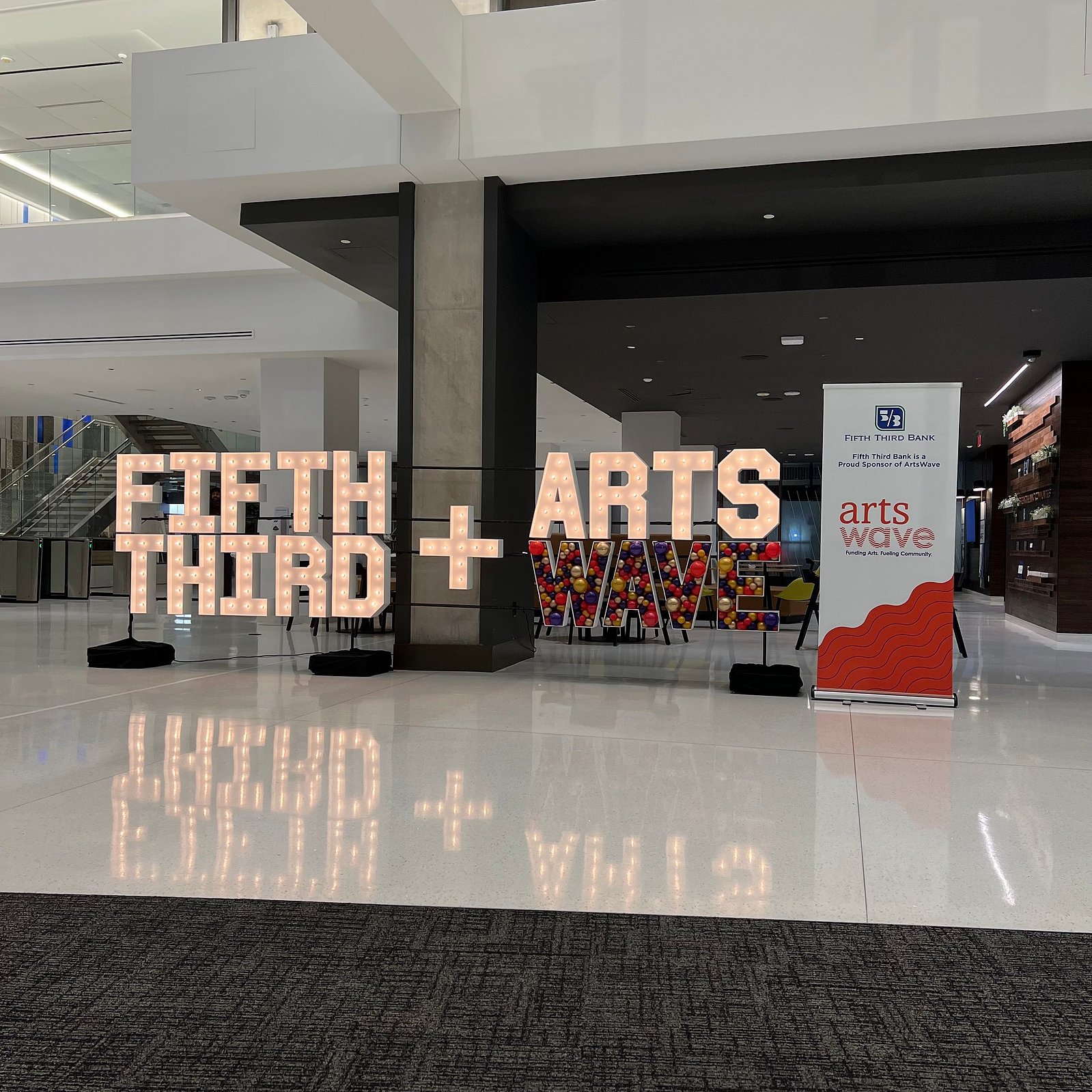 In a large open white room are light up marquee letters with balloon mosaic letters next to an event sign