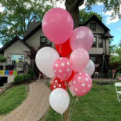In the front lawn of a home is a helium balloon bouquet of pink white red and polka dot balloons