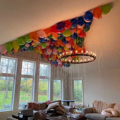 resting on the ceiling of a living room are many helium balloons in every color