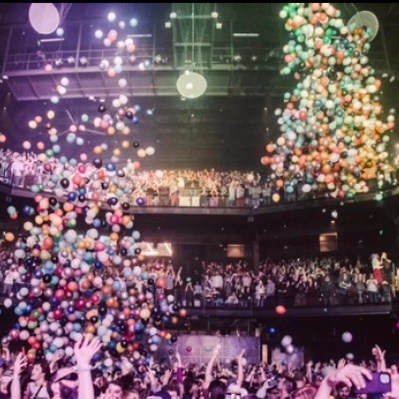 a large room filled with people lifting their hands as balloons fall from the ceiling