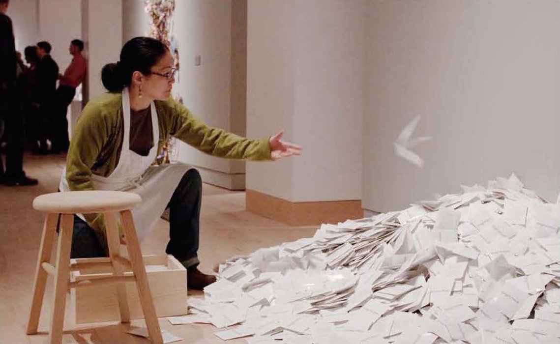 After filling three seed packets, Li Chiao-Ping tosses them onto the heap of filled packets already prepared by other volunteers. In mid-air the packets form the shape of a bird released from her hand.  