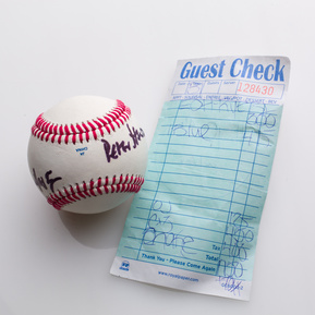 photograph of ephemera from douglas rosenberg's relational performance, containing a baseball signed by all participants in the performance and the bill for the breakfast