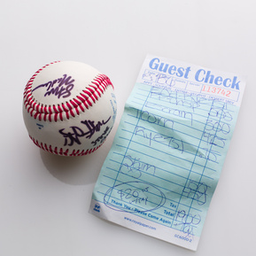 photograph of ephemera from douglas rosenberg's relational performance, containing a baseball signed by all participants in the performance and the bill for the breakfast