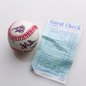 photograph of ephemera from douglas rosenberg's relational performance, containing a baseball signed by all participants in the performance and the bill for the breakfast