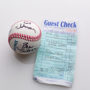 photograph of ephemera from douglas rosenberg's relational performance, containing a baseball signed by all participants in the performance and the bill for the breakfast