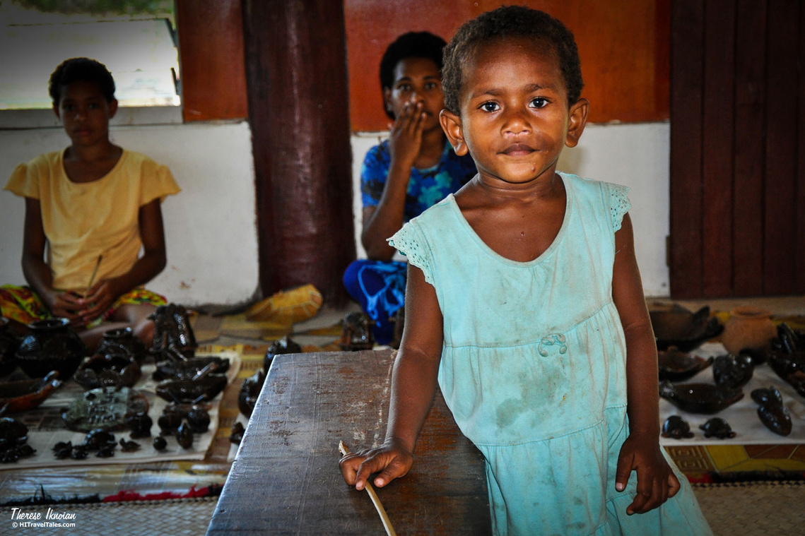 A little girl in Fiji in a pottery-making village, staring at the camera. 