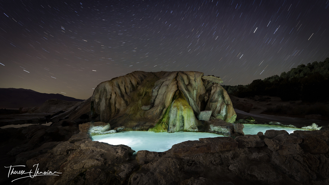 Night photo of hot springs near Bridgeport, California, with star trails and the water illuminated. 
