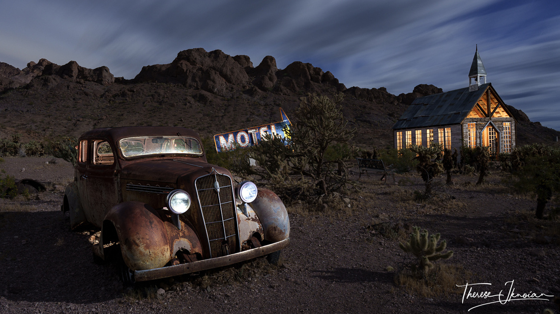 Night photo of Nelson Ghost Town in Nevada with a church, sign and old car light painted. 