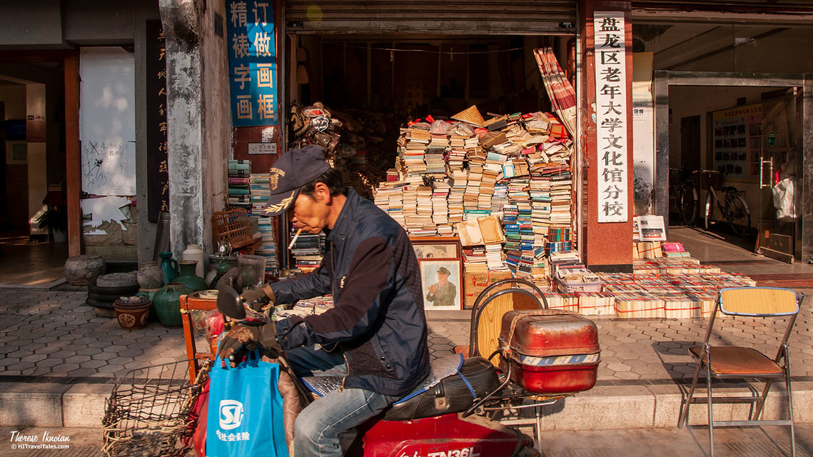 Man on a motorbike passing a bookstore stacked with books during golden hour in Kunming, China. 