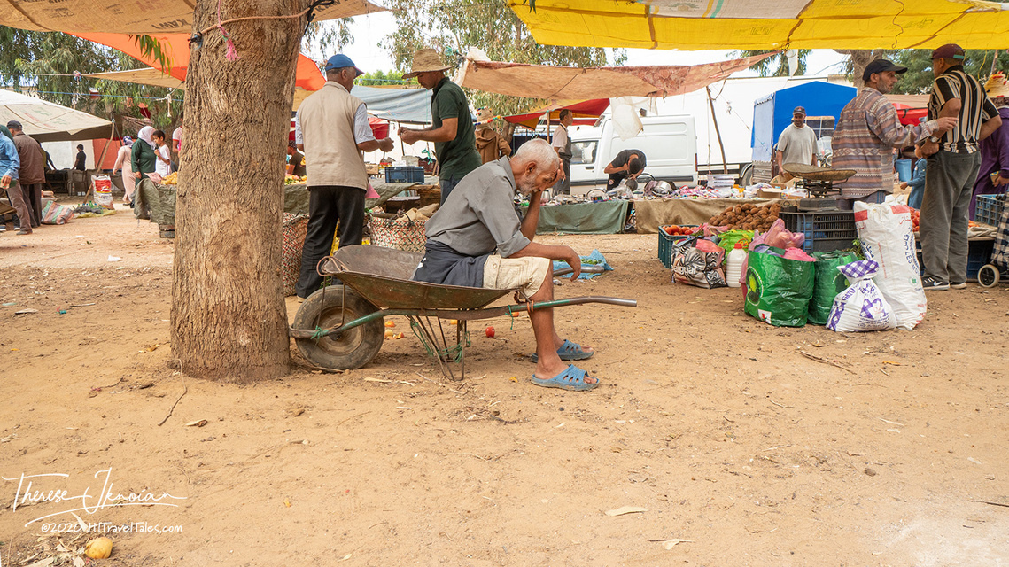 An exhausted man sits in a wheelbarrow with his head in a hand in a regional market in Morocco. 
