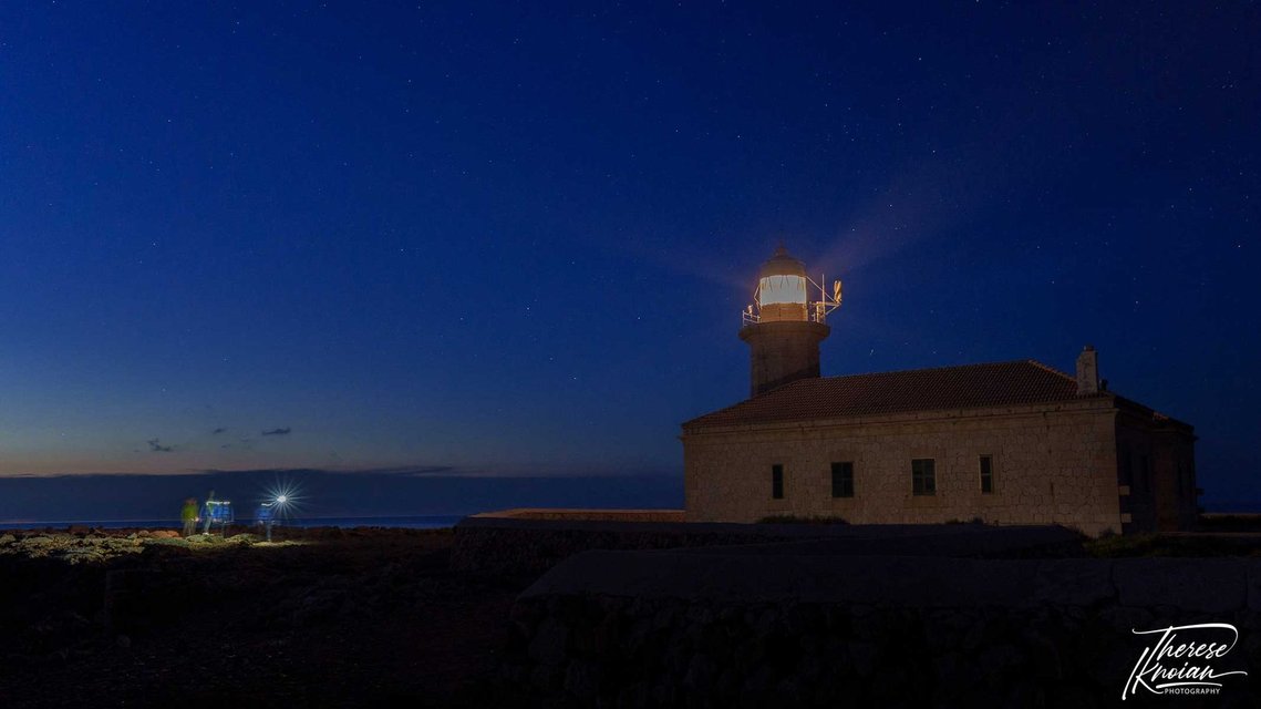 Passers-by wearing headlamps near a lighthouse in Menorca.