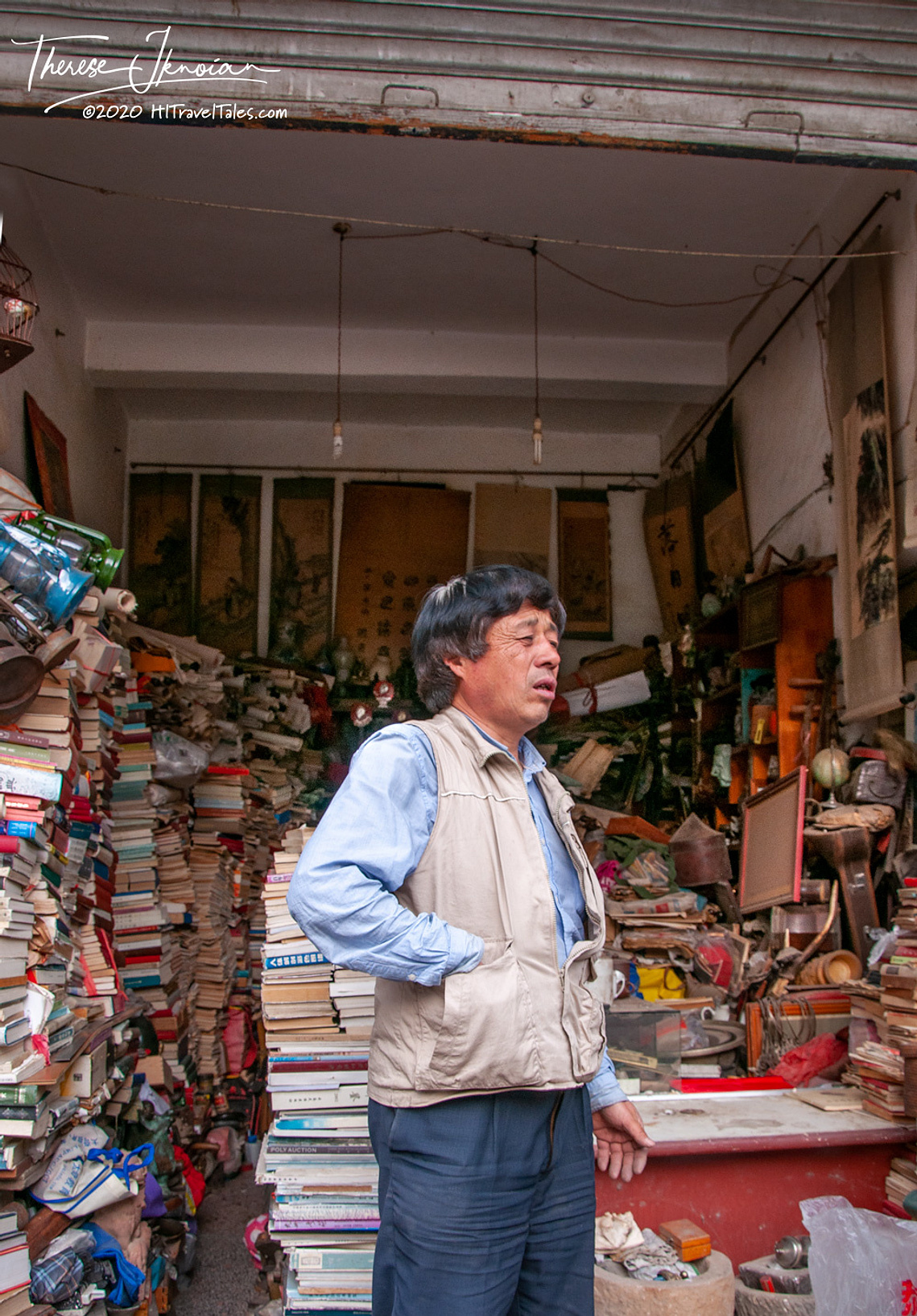 A bookstore owner standing in front of a crazy pile of books in Kunming, China. 