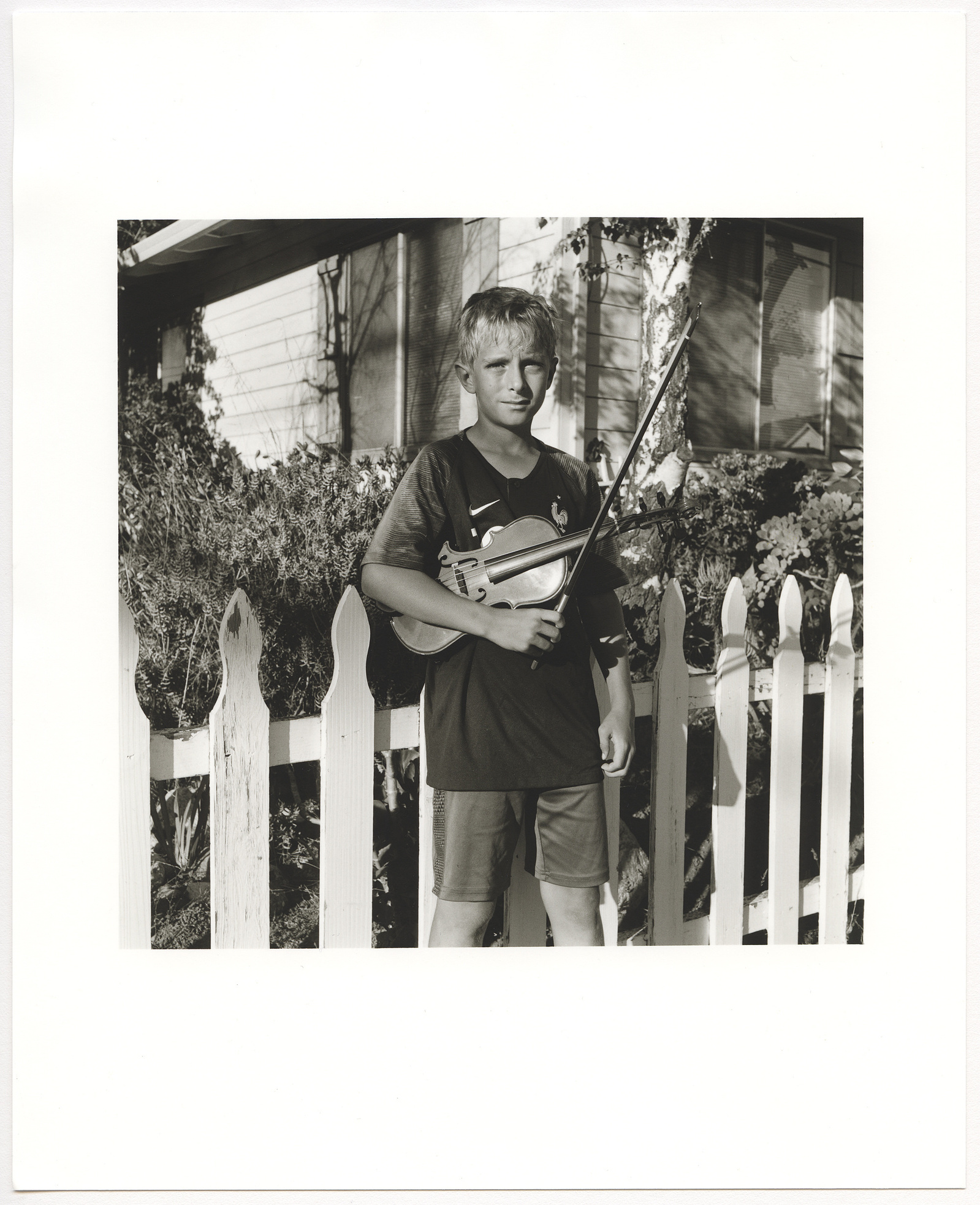 Boy with his violin in front of a picket fence.