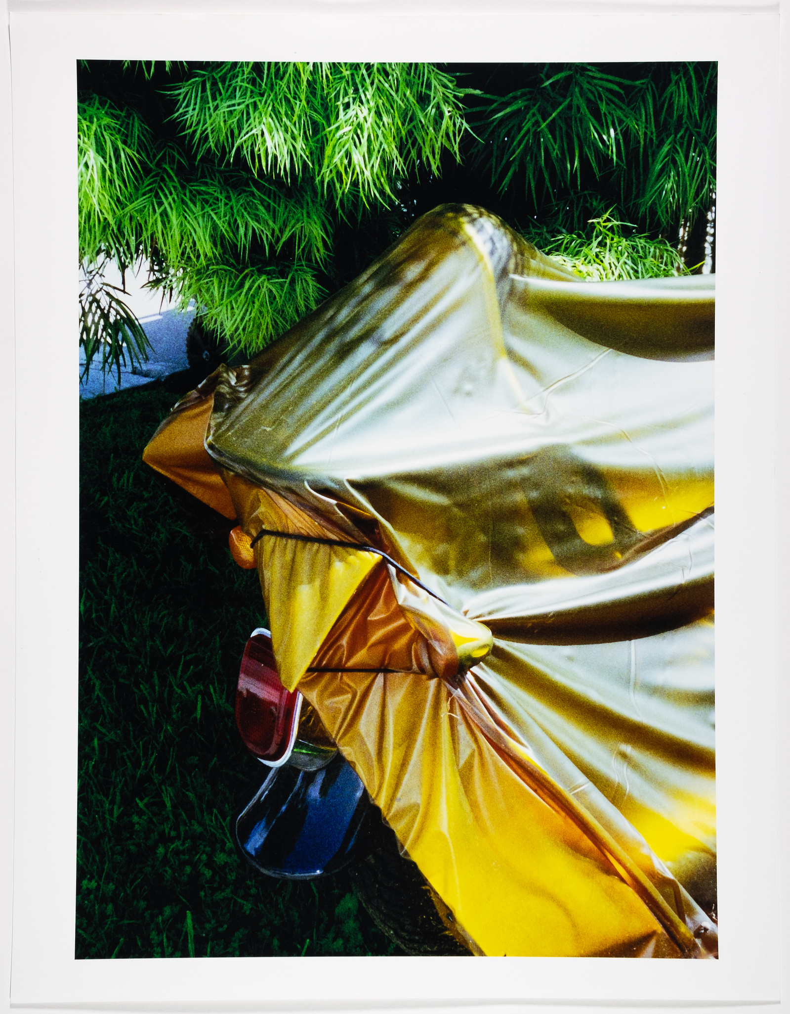 A motorcycle wrapped in a yellow tarp next to a bush