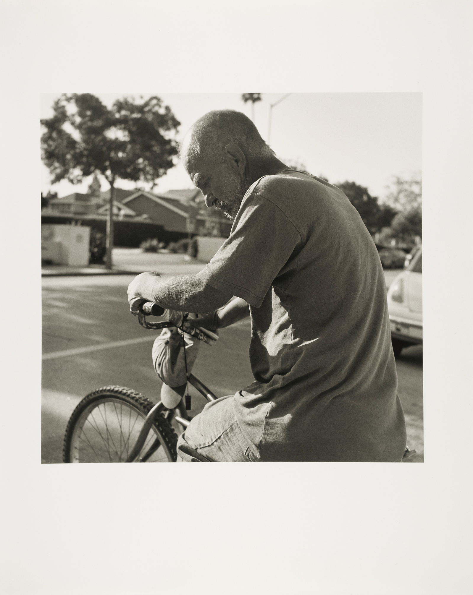 An older man with a buzzed head on his bicycle, at rest
