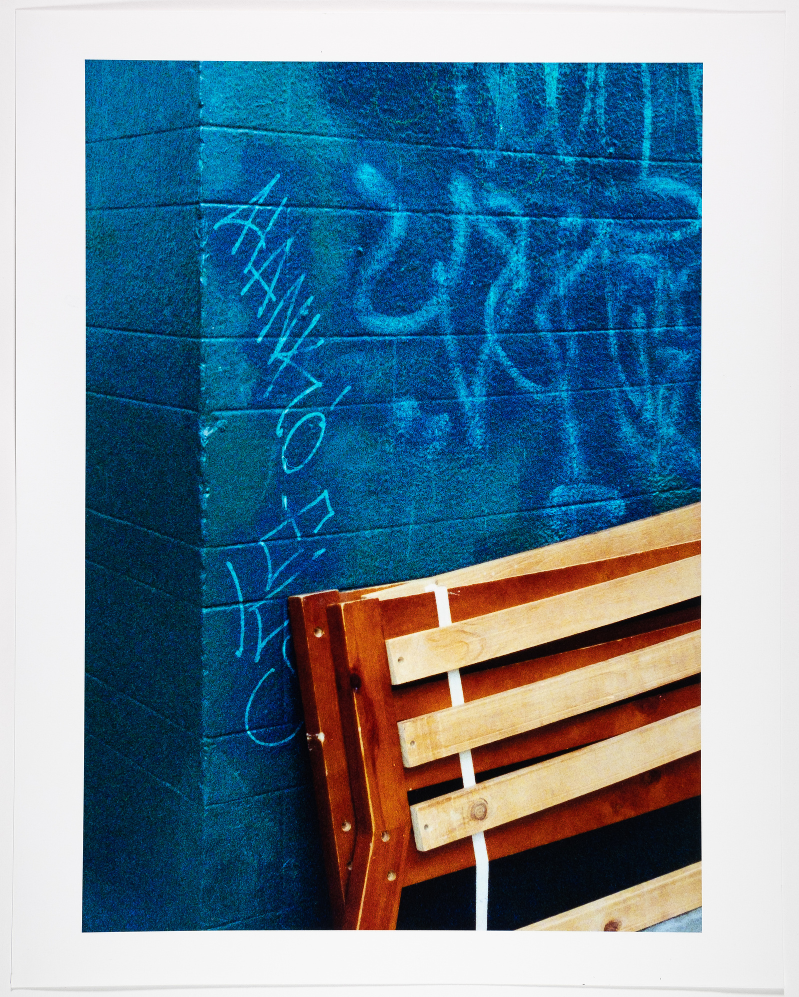 Abstracted street scene. Discarded furniture leans against a blue graffiti wall