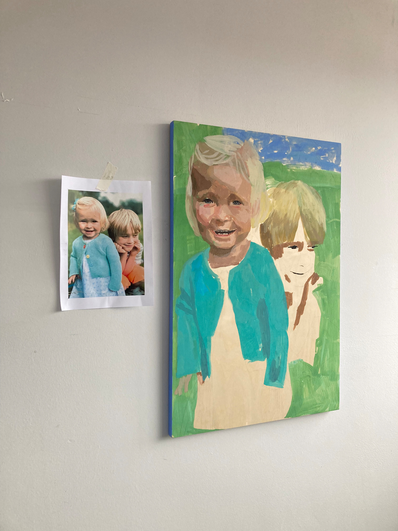 A process photograph of a painted portrait and its reference photograph. It depicts a young brother and sister. The painting is made by the female British artist Mary Naylor in her Scarborough Studio