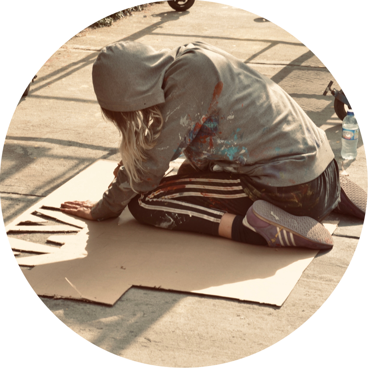 Artist Mary Naylor, sitting on a street floor in Bogotá Colombia cutting out a stencil. 2019