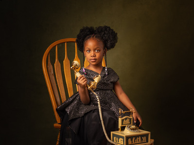 Portrait of a little girl holding an analog rotary phone while sitting on a chair against a green canvas backdrop