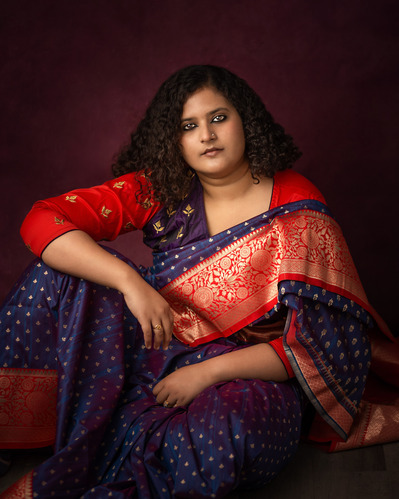 Portrait of a beautiful Indian lady wearing her traditional outfit against a maroon backdrop
